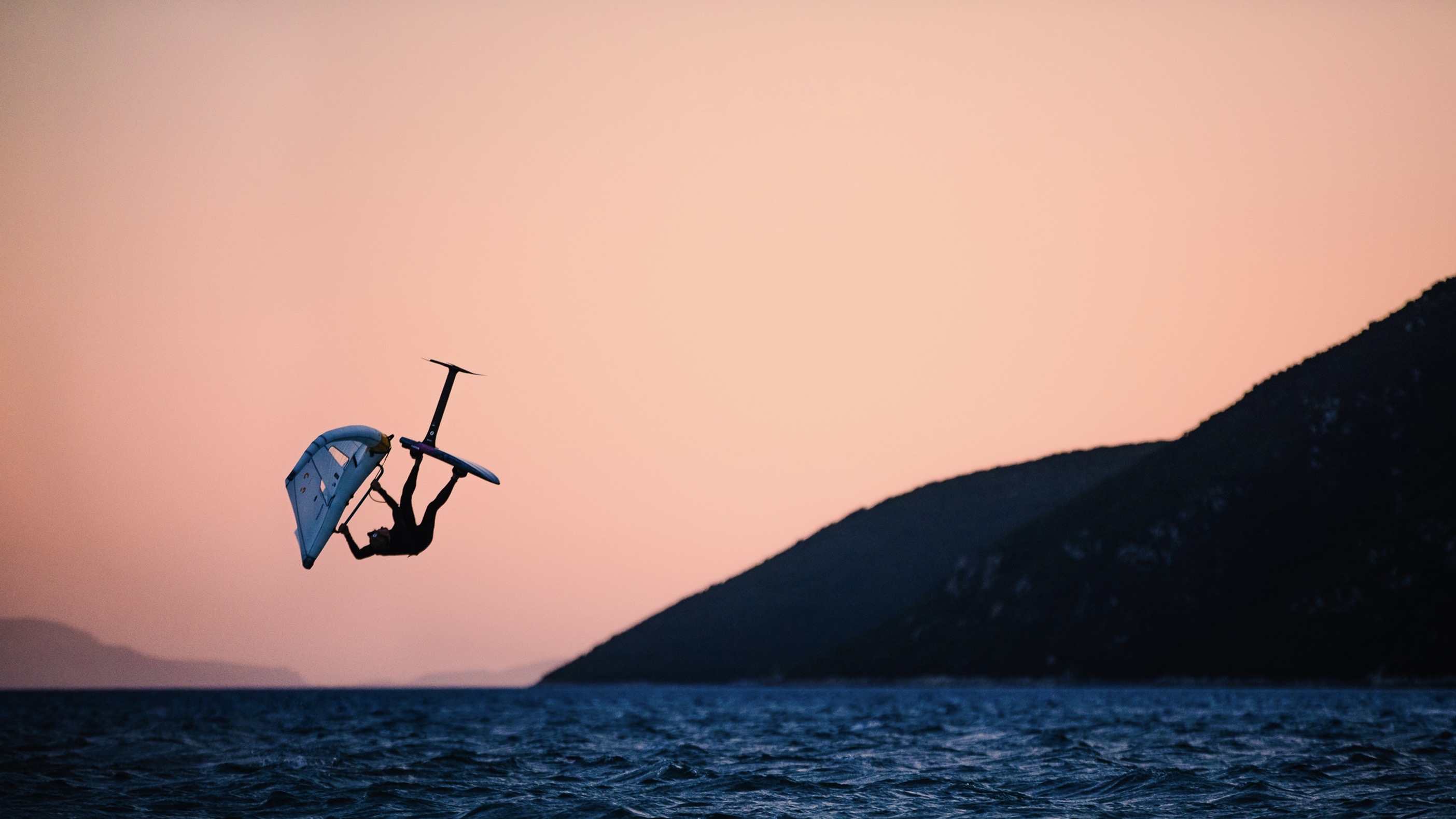 Toby Cunliffe mid-flip on a wing foil at sunset